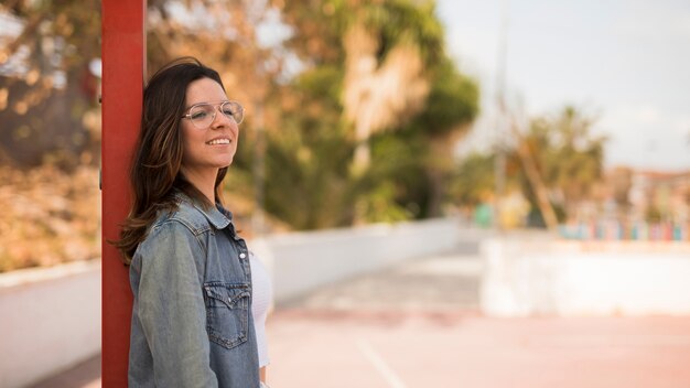 Ritratto sorridente degli occhiali d&#39;uso di una giovane donna che si appoggia palo