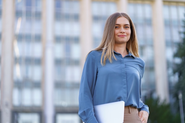 Ritratto sorridente della giovane donna bionda che indossa camicia delicata blu sopra la costruzione