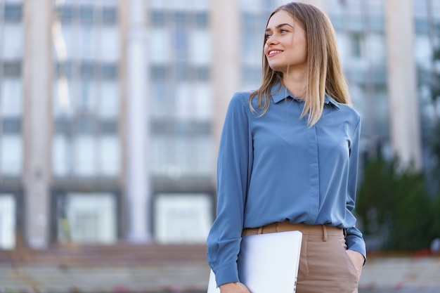 Ritratto sorridente della giovane donna bionda che indossa camicia delicata blu sopra la costruzione