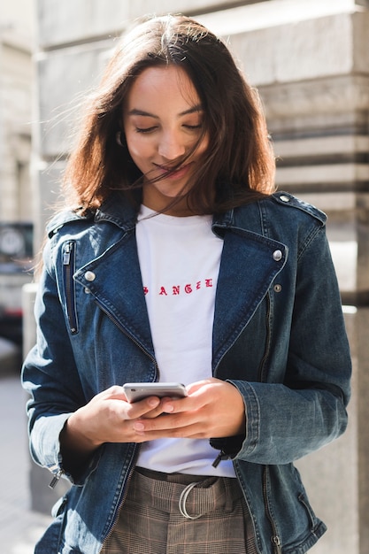 Ritratto sorridente di giovane donna alla moda che per mezzo del telefono cellulare