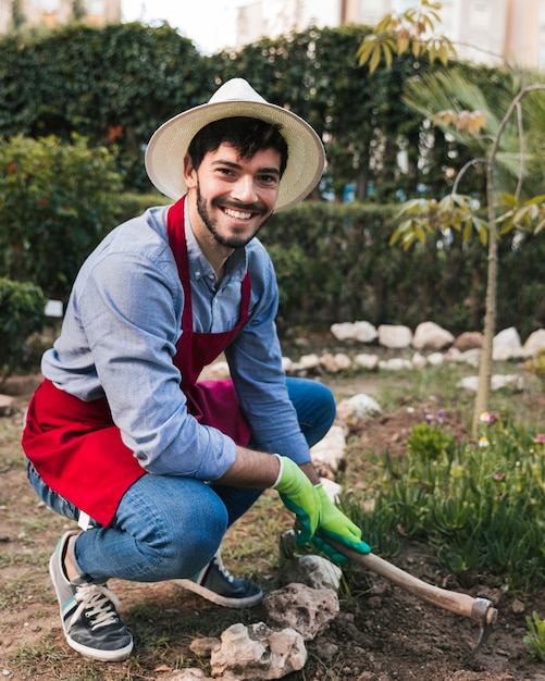 Ritratto sorridente di un giardiniere maschio che scava il suolo con la zappa nell&#39;orto