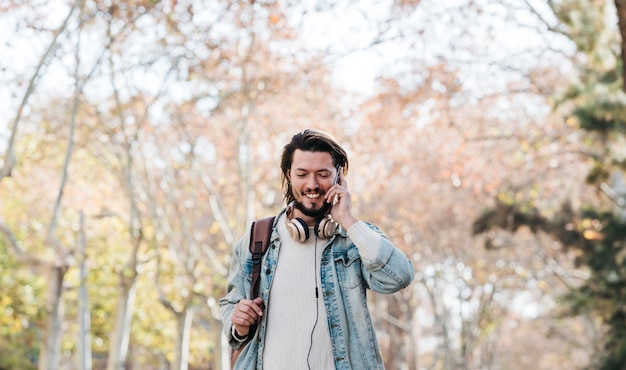 Ritratto sorridente di un giovane che cammina con il suo zaino che parla sul telefono cellulare nel parco
