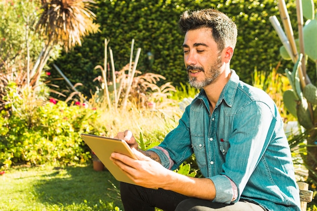 Ritratto sorridente di un uomo che utilizza compressa digitale nel parco