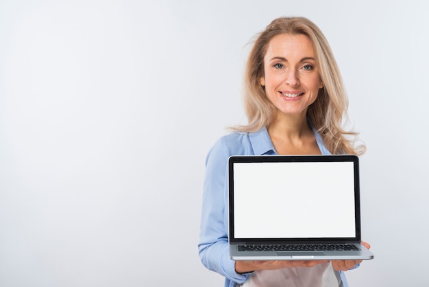 Ritratto sorridente di una giovane donna bionda che mostra computer portatile con esposizione in bianco sulla sua mano