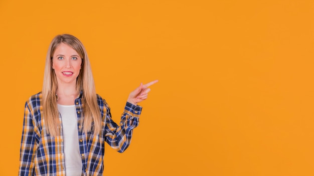 Ritratto sorridente di una giovane donna che indica il suo dito qualcosa su fondo arancio