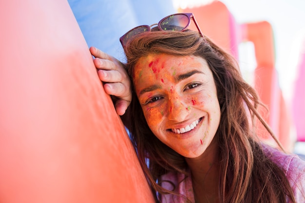 Ritratto sorridente di una giovane donna con i colori di holi su cipria che esamina macchina fotografica