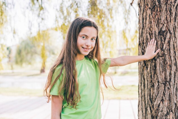 Ritratto sorridente di una ragazza che tocca la sua mano sul tronco d&#39;albero