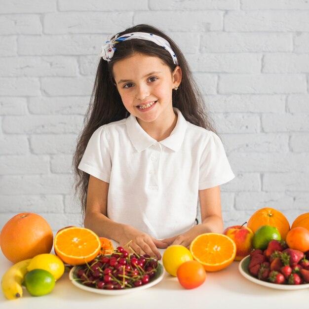 Ritratto sorridente di una ragazza con frutti colorati sulla scrivania