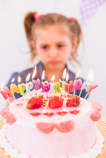 Ritratto vago di una ragazza triste che sta dietro la torta di compleanno della fragola