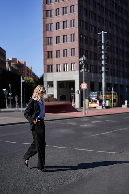 Ritratto verticale di donna d'affari sicura ed elegante in giacca e cravatta che cammina attraversando la strada nella città ce