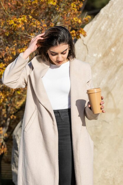 Ritratto verticale di giovane bella ragazza che tiene tazza di caffè Modello di moda donna ritratto di bellezza all'aperto Foto di alta qualità