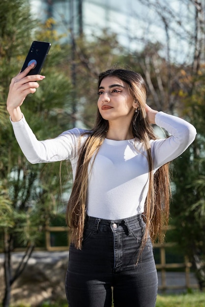 Ritratto verticale di giovane ragazza che prende selfie Foto all'aperto di giovane donna Foto di alta qualità