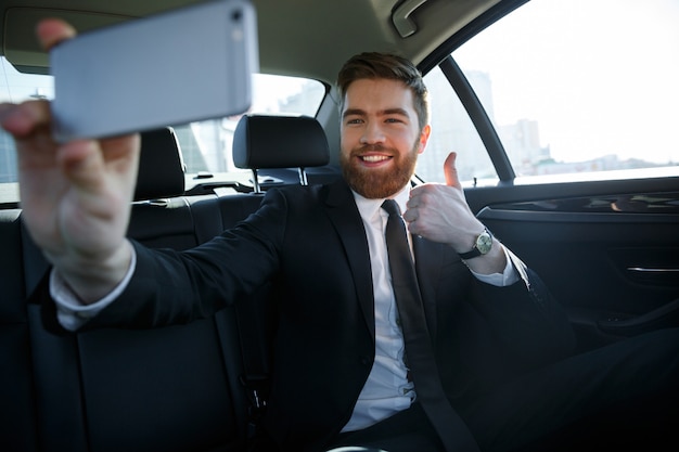 Riuscito uomo sorridente di affari che prende selfie