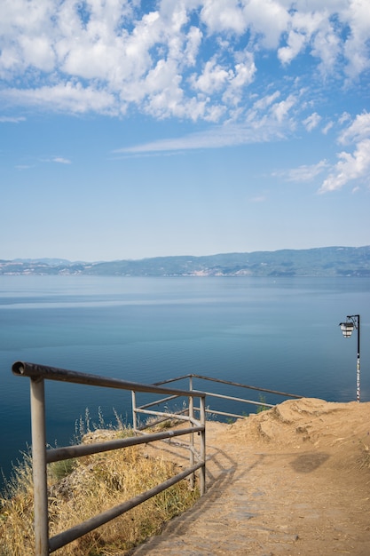 Riva con recinzioni metalliche circondata dal mare con le montagne sullo sfondo