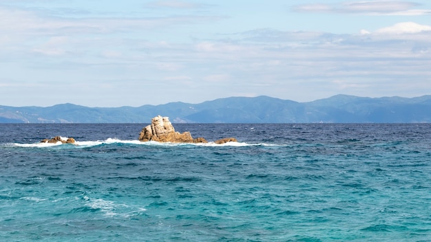 Rocce nelle acque del Mar Egeo con terra in lontananza in Grecia