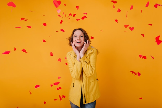 Romantica ragazza bianca con l'espressione del viso carino in posa con cuori rossi. Foto dell'interno della giovane donna riccia che celebra il giorno di San Valentino con il sorriso.