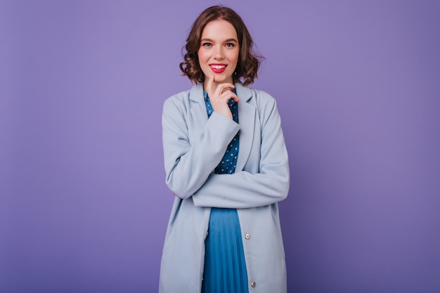 Romantica ragazza bianca con trucco alla moda in posa in cappotto. sorridente donna beata in abbigliamento blu.