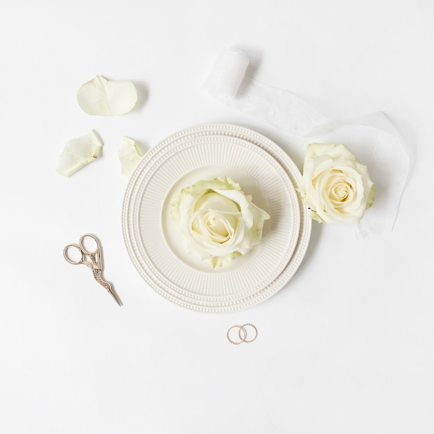 Rosa fresca sul piatto con nastro; Scissor e fedi nuziali su sfondo bianco
