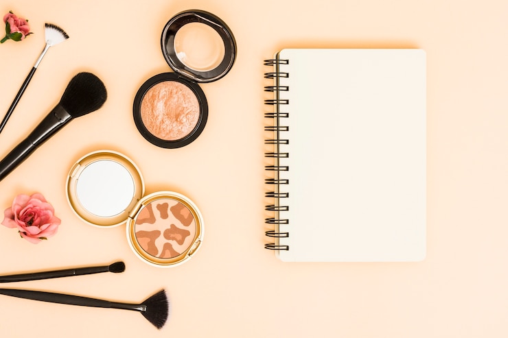 Foto gratuito rosa; pennelli per il trucco e polvere compatta vicino al blocco note a spirale sul fondale beige