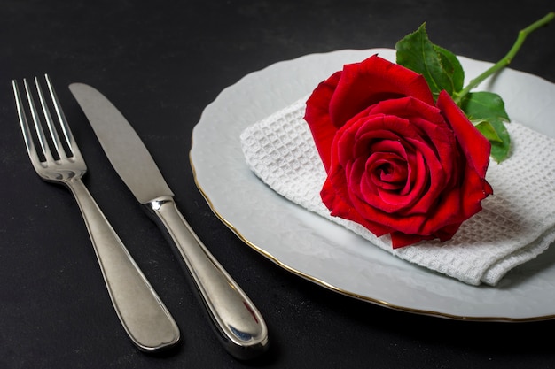 Rosa rossa del primo piano su un piatto con la coltelleria