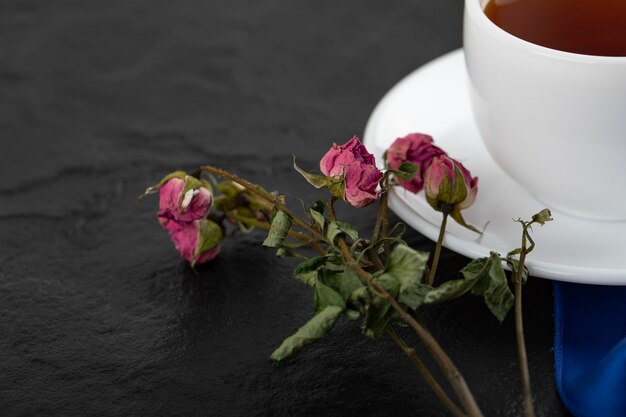 Rose secche con una tazza di tè caldo su un tavolo nero.