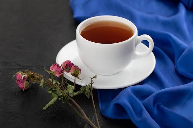 Rose secche con una tazza di tè caldo su un tavolo nero.