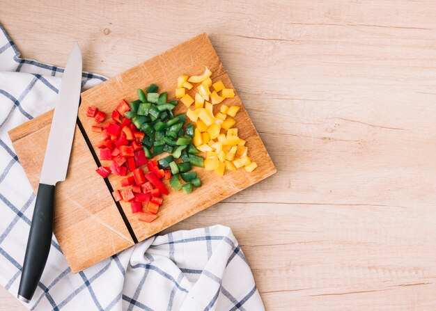 Rosso biologico fresco tritato; peperoni gialli e verdi sul tagliere con coltello sopra la scrivania in legno