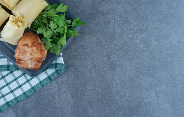 Rotoli di pasta bolliti e pollo arrosto su tavola scura.