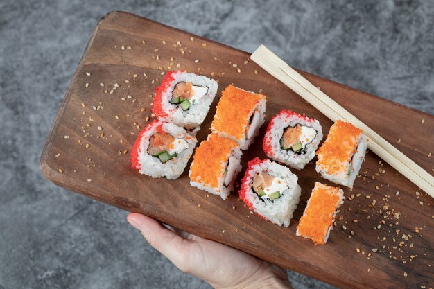 Rotoli di sushi con caviale giallo e rosso su una tavola di legno.