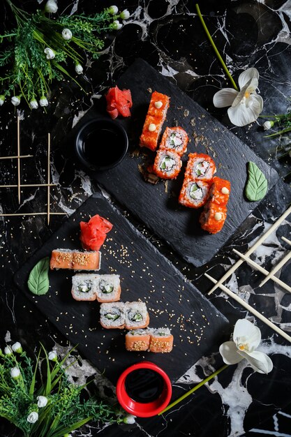 Rotoli di sushi della California di vista superiore con i rotoli di Philadelphia sui supporti con wasabi della salsa di soia e zenzero con i fiori