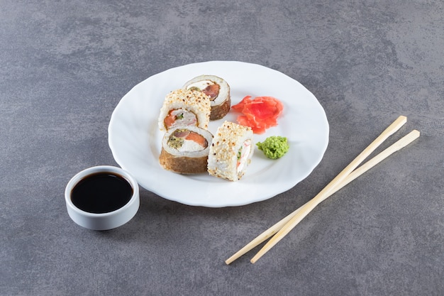 Rotoli di sushi, salsa di soia, wasabi e zenzero sottaceto sulla superficie di pietra.