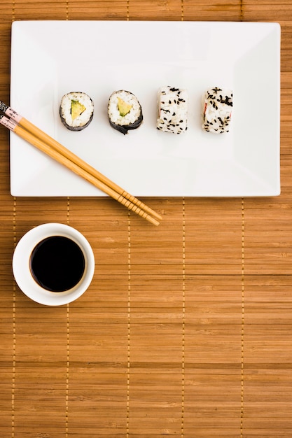 Rotoli di sushi sani sul piatto con le bacchette e salsa di soia scura sopra tovaglietta