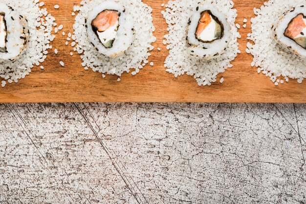 Rotolini di sushi disposti su riso crudo sopra il vassoio di legno