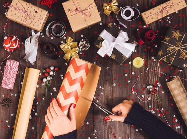 Rotolo della tenuta della mano della donna della carta da imballaggio di Kraft con le forbici per il taglio del contenitore di regalo di natale dell&#39;imballaggio