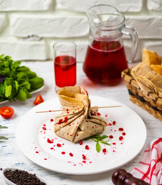 Rotolo di snack Lavash con formaggio e semi di granato, pane, verdure e sorbetto su un piatto bianco. Spuntino