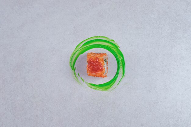 Rotolo di sushi della California su priorità bassa bianca con anello di plastica verde.