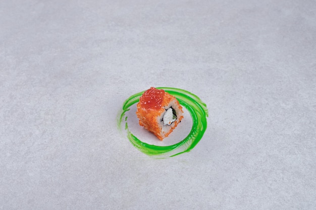 Rotolo di sushi della California su priorità bassa bianca con anello di plastica verde.