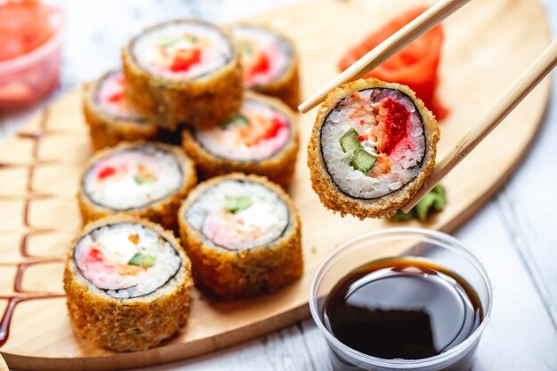 Rotolo di sushi fritto nel grasso bollente del rotolo caldo di vista laterale con lo zenzero e il wasabi di color salmone del pomodoro del cetriolo del formaggio cremoso su un bordo