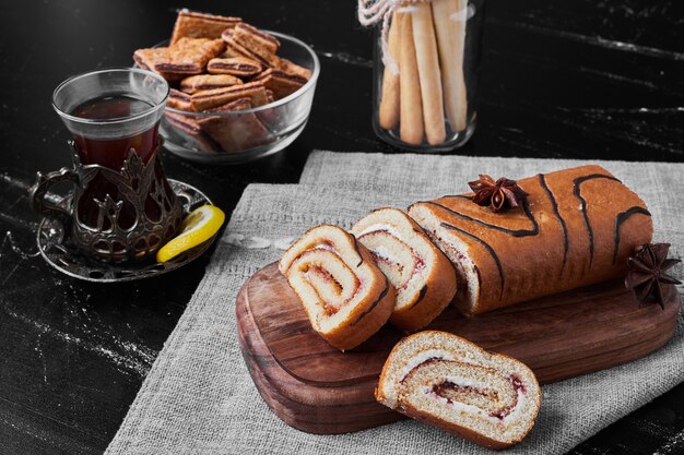 Rotolo di torta affettata su una tavola di legno e servita con un bicchiere di tè.