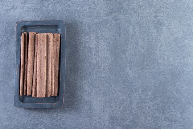 Rotolo di wafer al cioccolato gustoso in un piatto di legno, sullo sfondo di marmo.