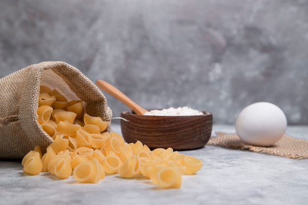 Sacco di maccheroni secchi a forma di conchiglia con una ciotola di legno di farina