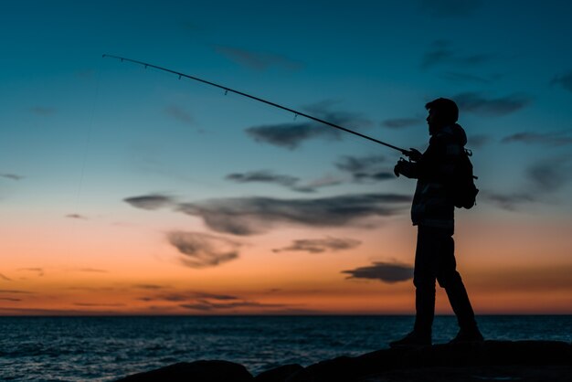 Sagoma di un uomo che pesca in spiaggia al tramonto