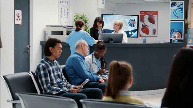 Sala d'attesa nella hall dell'ospedale con banco della reception, diverse persone in attesa di partecipare all'appuntamento per la visita di controllo. Esame sanitario in area di emergenza presso la clinica medica.