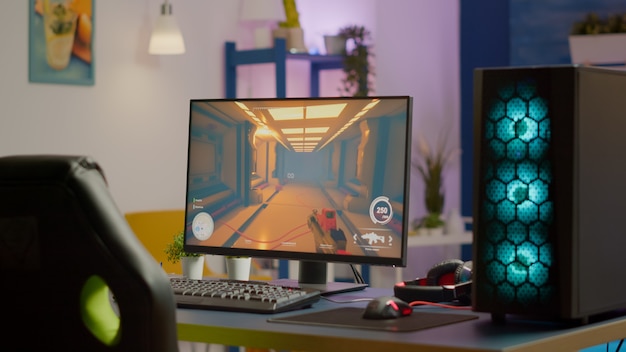 Sala giochi senza persone dotata di potente personal computer RGB per tornei di videogiochi online e sedia da gioco, gioco sparatutto in prima persona su schermo. Stanza accogliente con luce al neon.