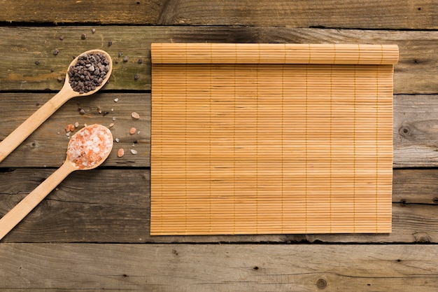 Sale rosa e nero in cucchiai di legno con tappetino su fondo di legno