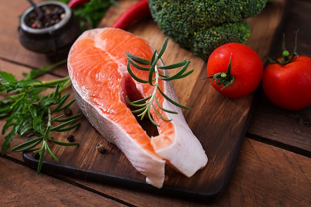 Salmone e verdure crudi della bistecca per la cottura sulla tavola di legno in uno stile rustico.