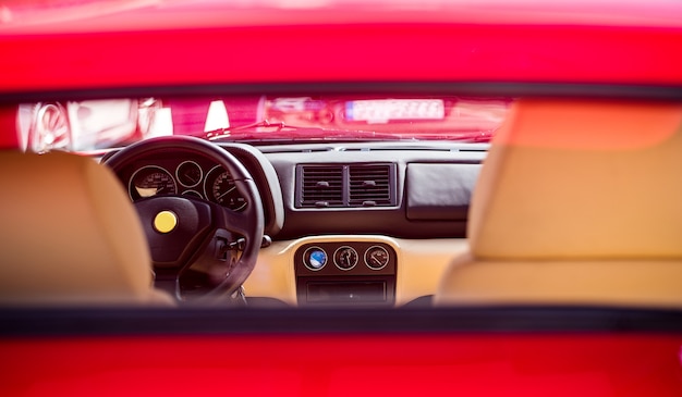 Salone di automobile sportiva rosso, direzione vire, interno in pelle marrone.