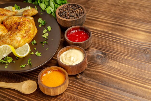 Salse laterali vista ravvicinata e piatto di pollo di pollo e limone accanto a ciotole di tre tipi di salse e pepe nero e cucchiaio di legno