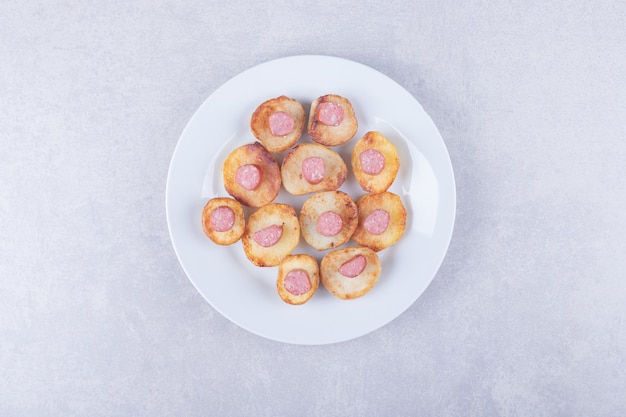 Salsicce affumicate con patate fritte sul piatto bianco.