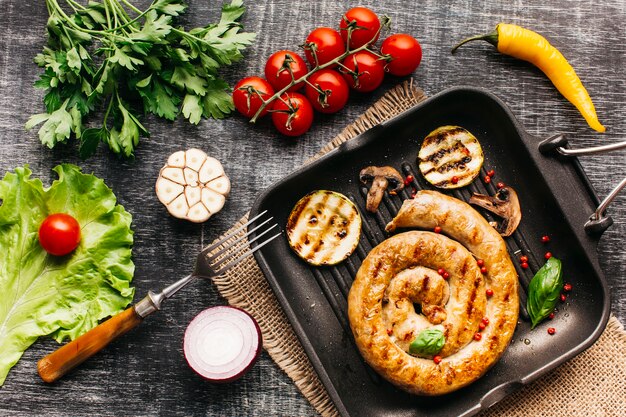 Salsicce alla lumaca alla griglia in padella con spezie e verdure su sfondo grigio in legno